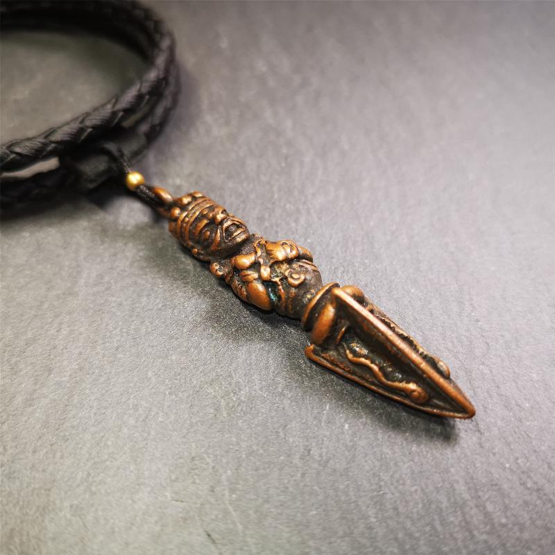This vintage Phurba pendant was collected from Rega Monastery(Baiyu,Tibet),handmade of copper. It has a statue of Vajrapani on the top and a phurba on the lower part, measuring about 2.36 inches by 0.47 inch.