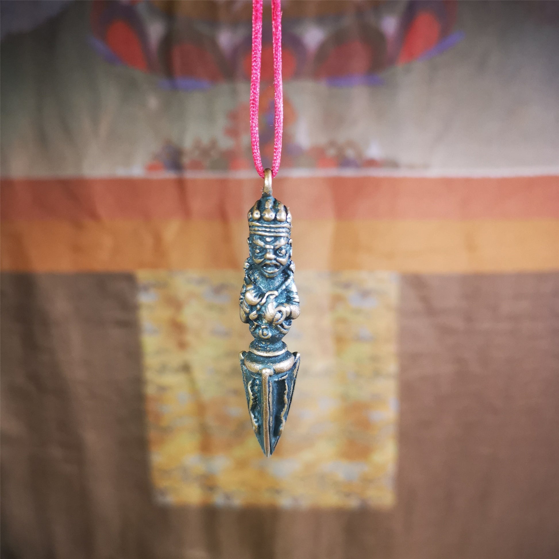 This vintage Phurba pendant was collected from Rega Monastery(Baiyu,Tibet),handmade of copper. It has a statue of Vajrapani on the top and a phurba on the lower part, measuring about 2.36 inches by 0.47 inch.