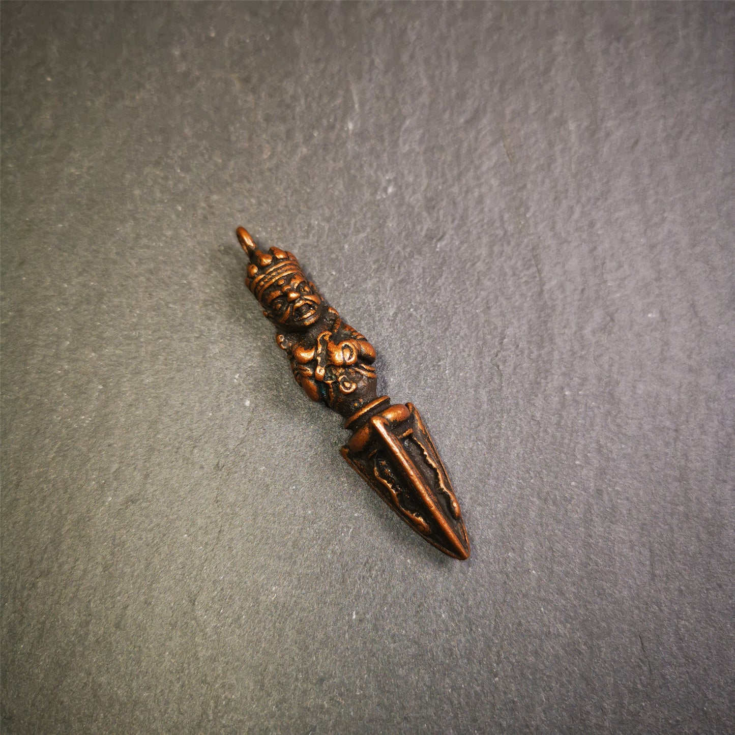 This vintage Phurba pendant was collected from Rega Monastery(Baiyu,Tibet),handmade of copper. It has a statue of Vajrapani on the top and a phurba on the lower part, measuring about 2.36 inches by 0.47 inch.