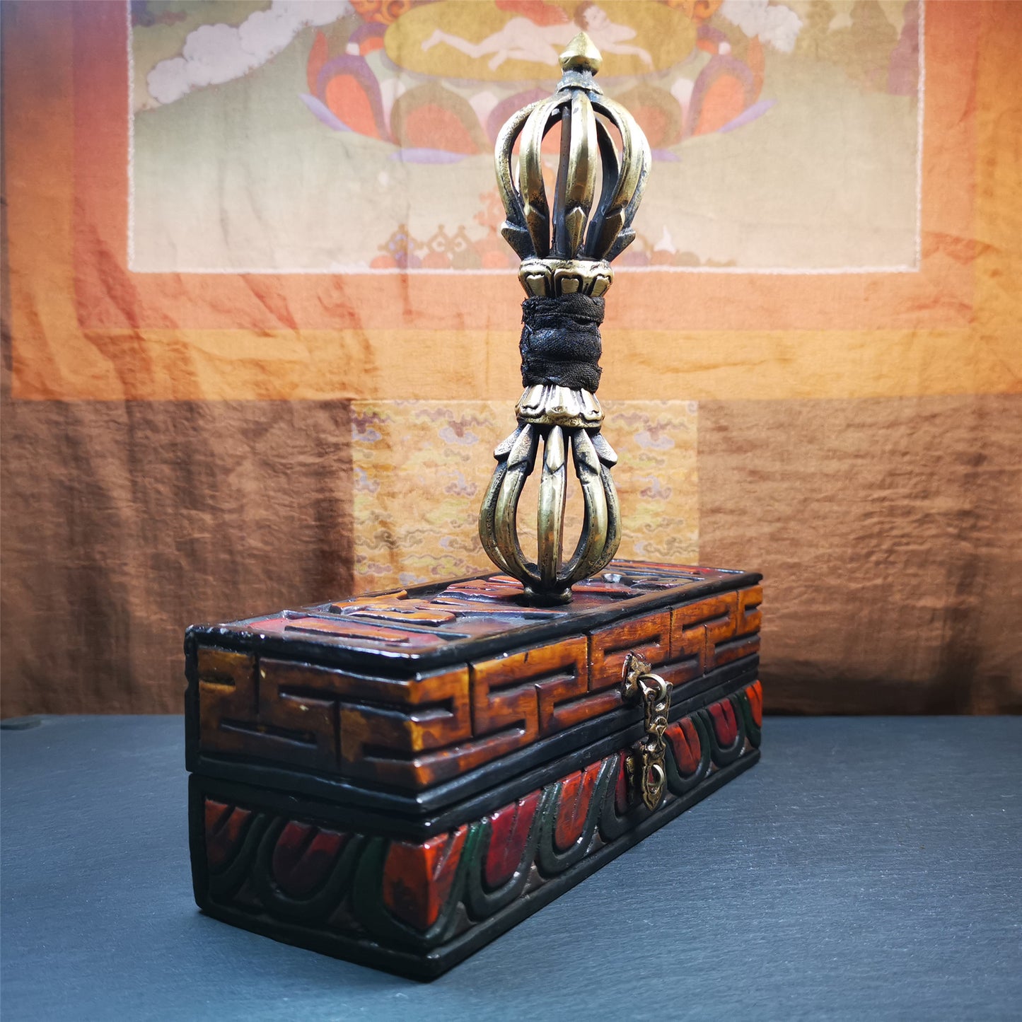 This vajra set was handmade in Nepal,using traditional techniques and materials. The Nine-pronged vajra is made of brass, and the outer box is made of wood,carved with the Tibetan letter of three karmas of word, thought , and deed The vajra can be inserted into the top of the box