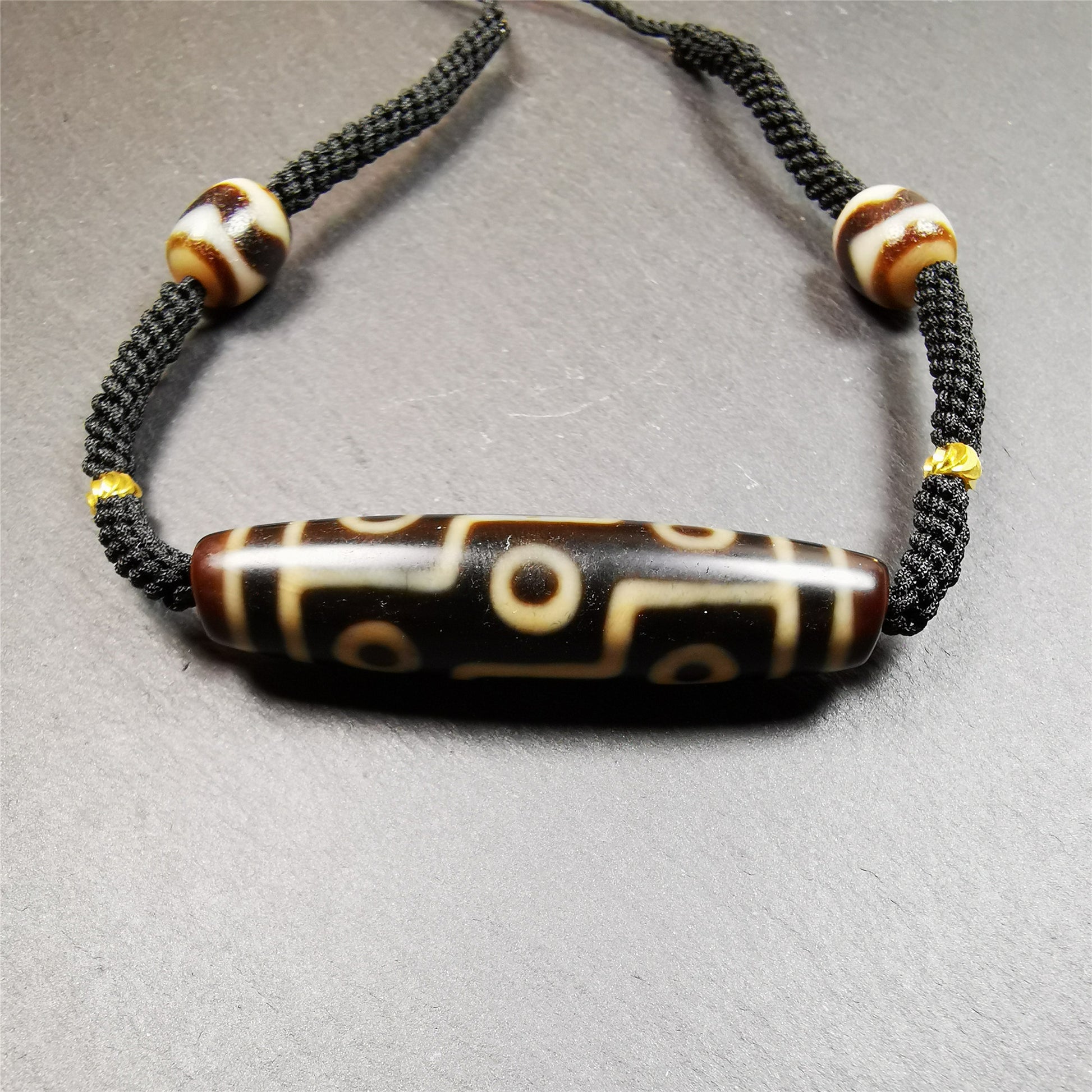 This necklace was hand-woven by Tibetans from Baiyu County, the main bead is a 9 eyed  dzi bead, paired with 2 small tiger tooth dzi beads,about 30 years old. It can be worn as a fashionable accessory,holds cultural and religious significance.