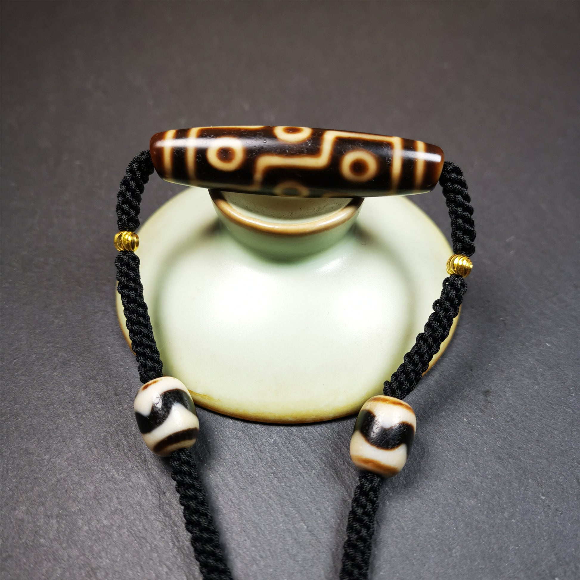 This necklace was hand-woven by Tibetans from Baiyu County, the main bead is a 9 eyed  dzi bead, paired with 2 small tiger tooth dzi beads,about 30 years old. It can be worn as a fashionable accessory,holds cultural and religious significance.