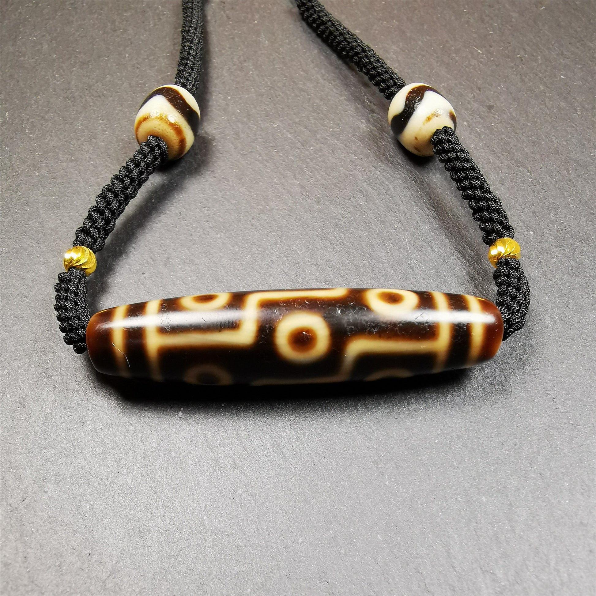 This necklace was hand-woven by Tibetans from Baiyu County, the main bead is a 9 eyed  dzi bead, paired with 2 small tiger tooth dzi beads,about 30 years old. It can be worn as a fashionable accessory,holds cultural and religious significance.