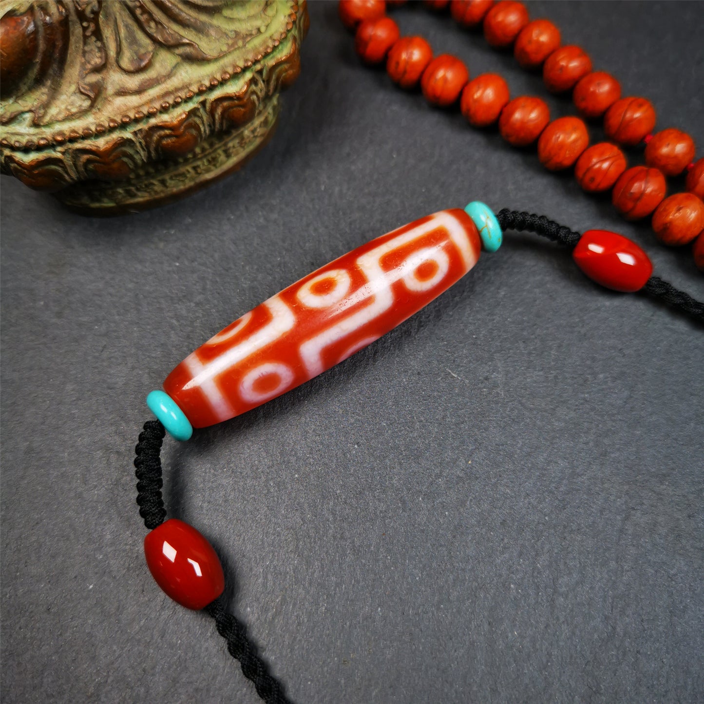 This fire agate 9 eyes dzi necklace was hand-woven by Tibetans from Baiyu County, the main bead is a fire agate 9 eyes dzi, paired with 2 turquoise beads and 2 red agate beads,about 30 years old. The length of the necklace can be adjusted, the maximum circumference is about 60cm.