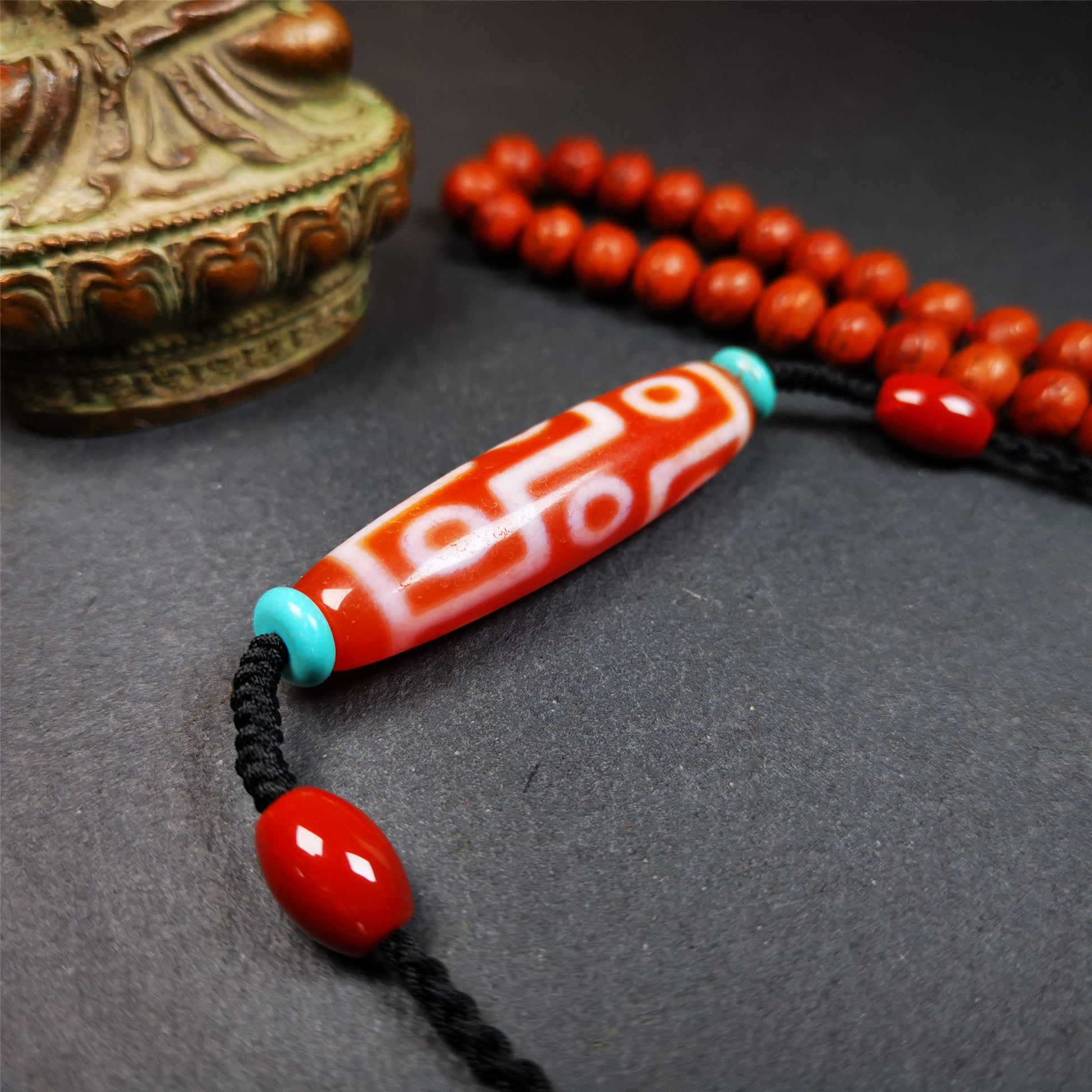 This fire agate 9 eyes dzi necklace was hand-woven by Tibetans from Baiyu County, the main bead is a fire agate 9 eyes dzi, paired with 2 turquoise beads and 2 red agate beads,about 30 years old. The length of the necklace can be adjusted, the maximum circumference is about 60cm.