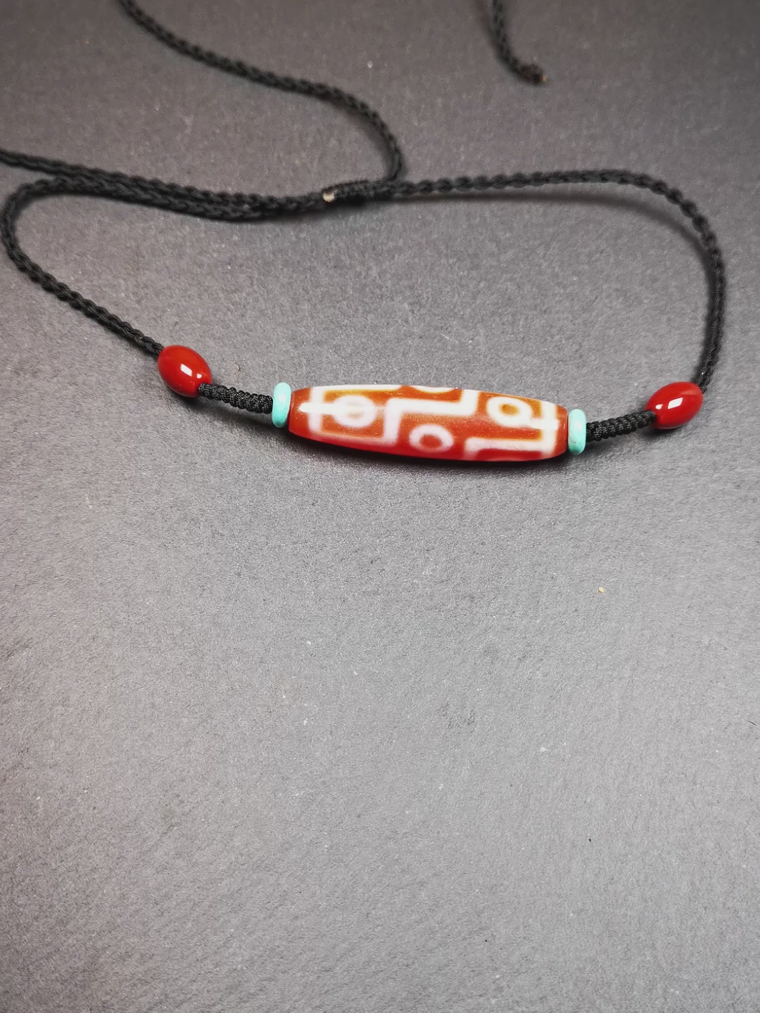 This fire agate 9 eyes dzi necklace was hand-woven by Tibetans from Baiyu County, the main bead is a fire agate 9 eyes dzi, paired with 2 turquoise beads and 2 red agate beads,about 30 years old. The length of the necklace can be adjusted, the maximum circumference is about 60cm.